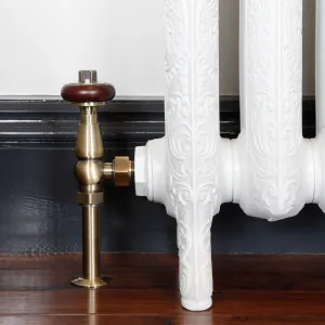 Windsor angled valve in Antique Brass with a wooden head, fitted to an ornate white cast iron radiator on feet beside a dark skirting board.