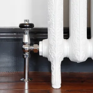 Chrome Windsor angled radiator valve with black wooden head fitted to an ornate white cast iron radiator on feet, by a dark skirting board.