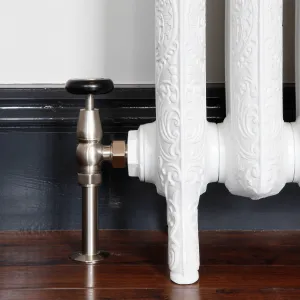 Windsor angled manual valve in Satin Nickel with a black wheel head, fitted to an ornate white cast iron radiator on feet beside a dark skirting board.