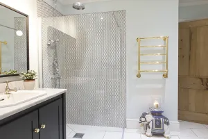 Wall-hung Elara towel rail with five gold bars beside a walk-in shower with penny tiles, next to a marble-topped navy vanity and oak door.