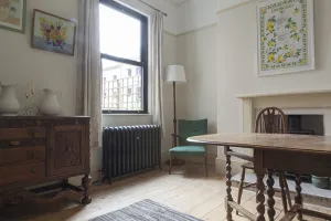 Ornate Rococo II cast iron radiator in dark grey sparkle on feet under a sash window, beside a green armchair and floor lamp on bare floorboards.
