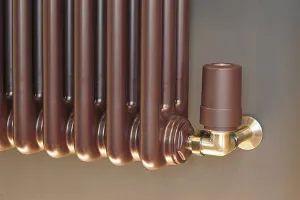 Close-up of the end of a plain Florence 3 column radiator in a metallic brown finish, with a brass angled valve and brown thermostatic head.